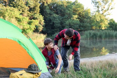 Photo of Father and son setting up camping tent near river outdoors