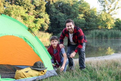 Photo of Happy father and son setting up camping tent near river outdoors