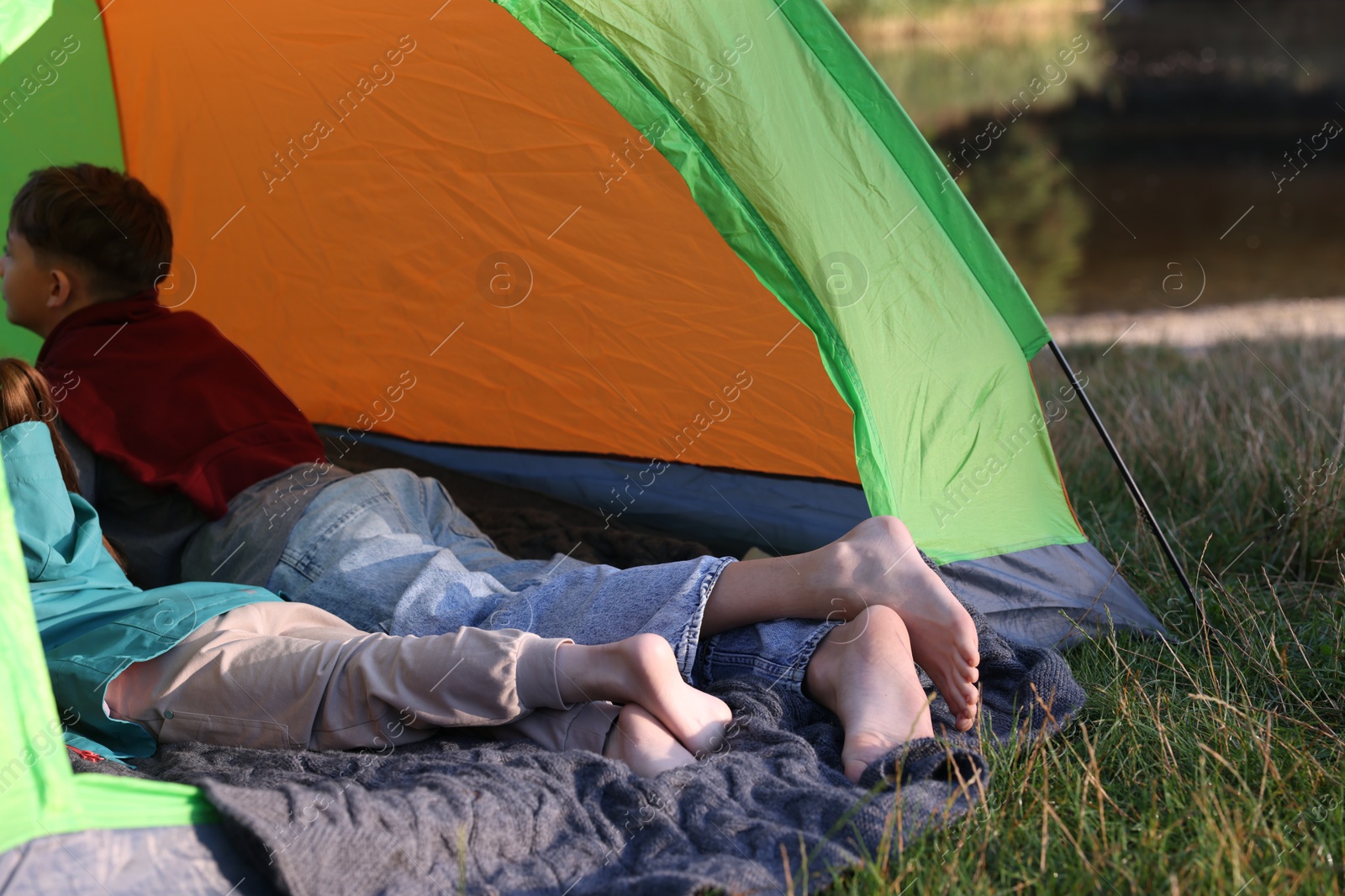 Photo of Brother and sister resting barefoot in camping tent outdoors, closeup