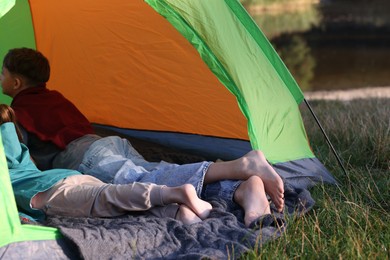 Photo of Brother and sister resting barefoot in camping tent outdoors, closeup