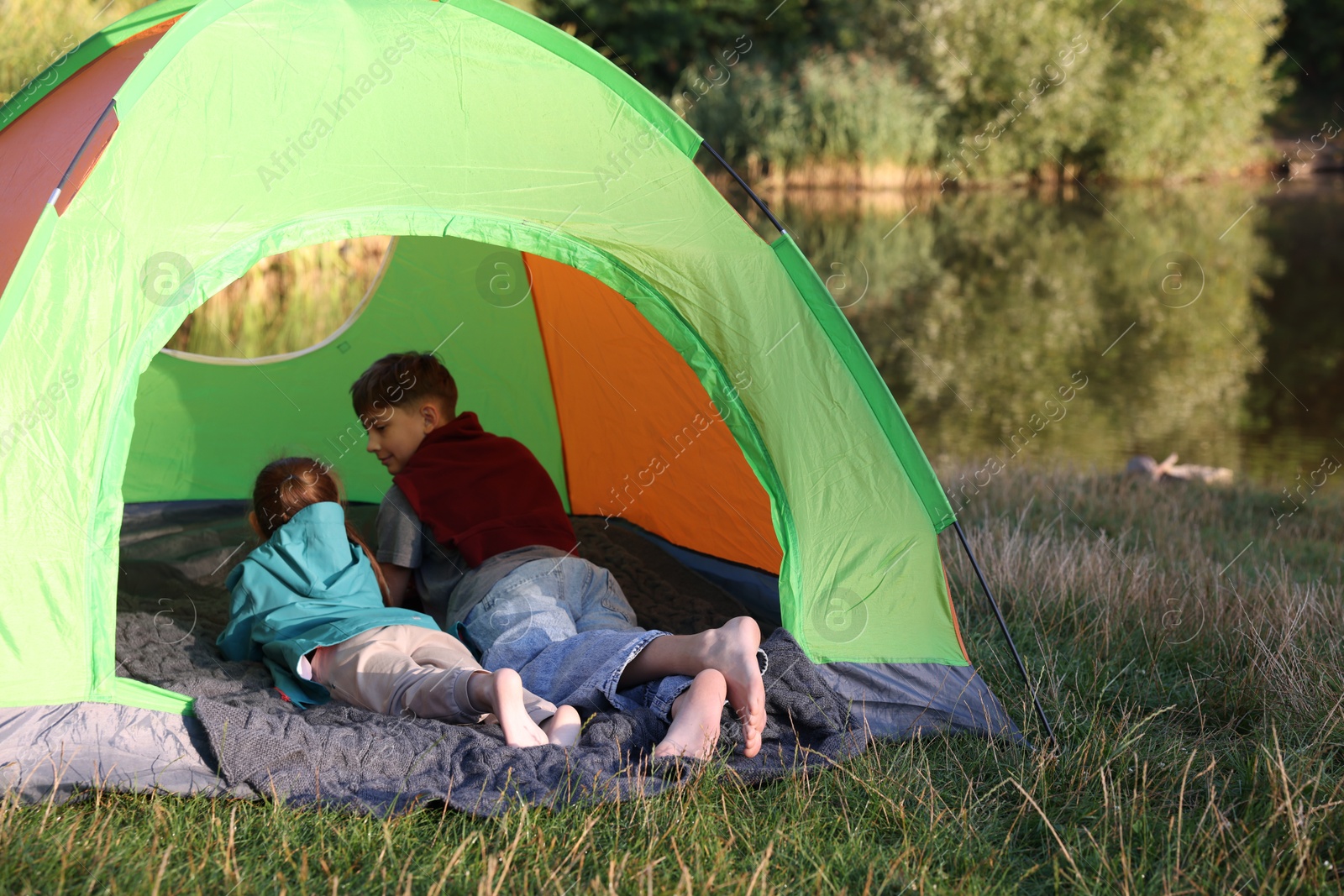 Brother and sister resting barefoot in camping tent near river outdoors. Space for text Photo of Brother and sister resting barefoot in camping tent near river outdoors. Space for text