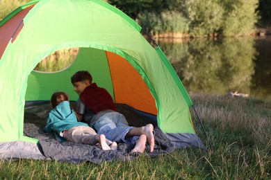 Photo of Brother and sister resting barefoot in camping tent near river outdoors. Space for text