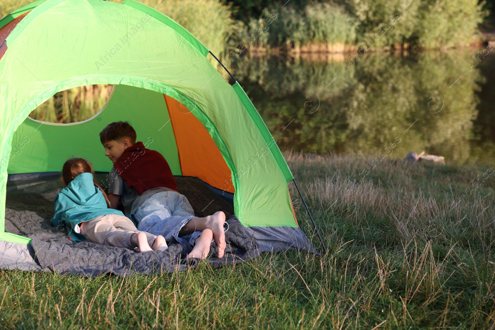 Photo of Brother and sister resting barefoot in camping tent near river outdoors. Space for text