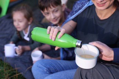 Photo of Mother pouring drink from bottle into mug and her children outdoors, closeup