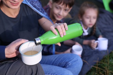 Photo of Mother pouring drink from bottle into mug and her children outdoors, closeup