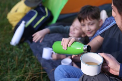 Photo of Mother pouring drink from bottle into mug and her children outdoors, closeup
