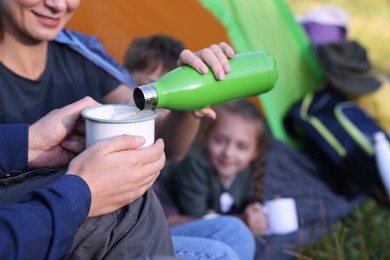 Photo of Mother pouring drink from bottle into mug and her children outdoors, closeup