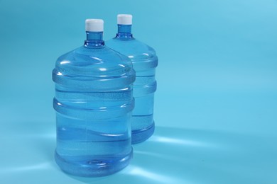 Photo of Cooler bottles with water on light blue background. Space for text
