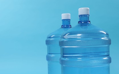 Photo of Cooler bottles with water on light blue background, closeup. Space for text