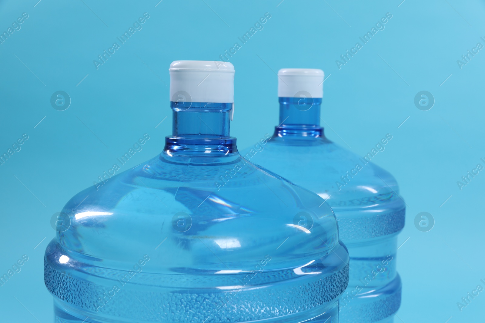 Cooler bottles with water on light blue background, closeup Photo of Cooler bottles with water on light blue background, closeup