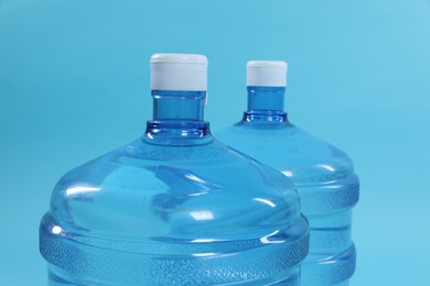 Photo of Cooler bottles with water on light blue background, closeup