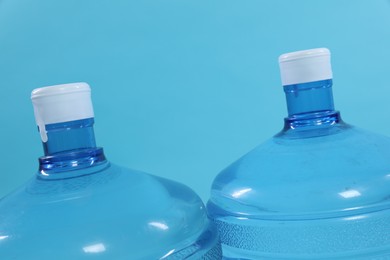 Photo of Cooler bottles with water on light blue background, closeup