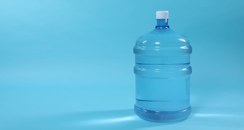 Photo of Cooler bottle with water on light blue background, closeup. Space for text