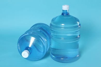 Photo of Cooler bottles with water on light blue background, closeup