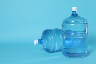 Photo of Cooler bottles with water on light blue background. Space for text
