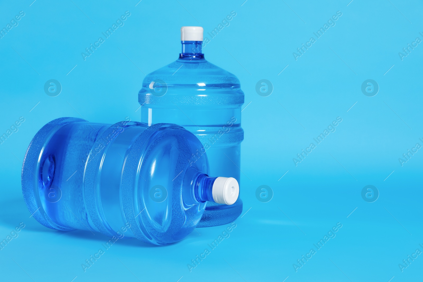 Cooler bottles with water on light blue background. Space for text Photo of Cooler bottles with water on light blue background. Space for text