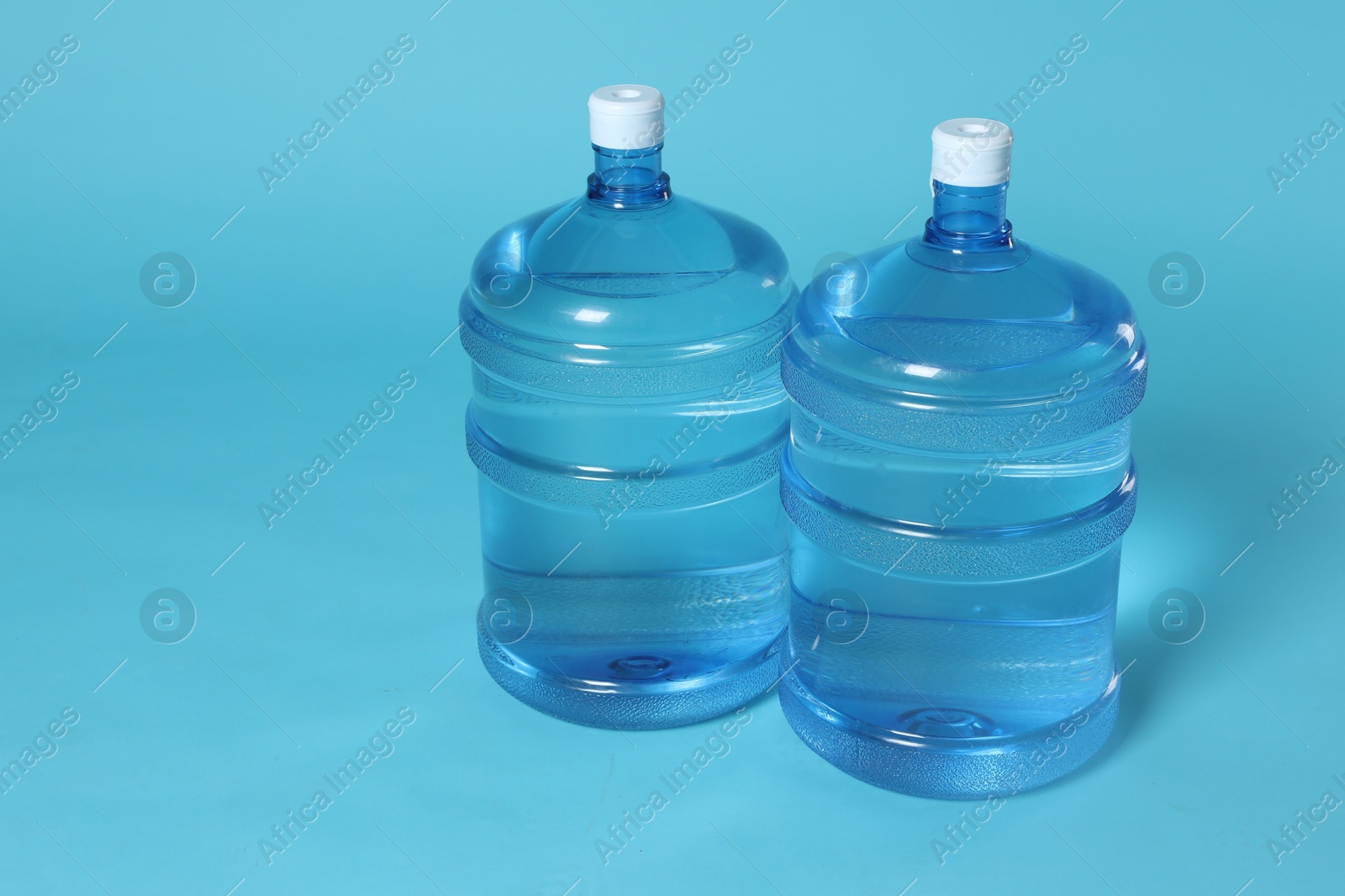 Cooler bottles with water on light blue background. Space for text Photo of Cooler bottles with water on light blue background. Space for text