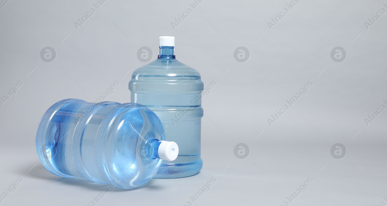 Photo of Cooler bottles with water on light grey background, closeup. Space for text