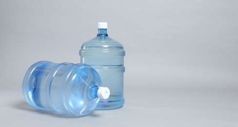 Photo of Cooler bottles with water on light grey background, closeup. Space for text