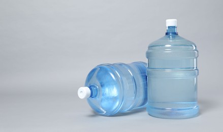 Photo of Cooler bottles with water on light grey background, closeup. Space for text
