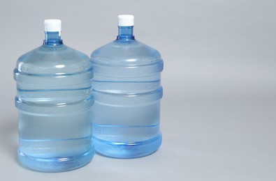 Photo of Cooler bottles with water on light grey background, closeup. Space for text