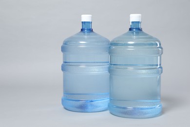 Photo of Cooler bottles with water on light grey background, closeup. Space for text