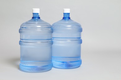 Photo of Cooler bottles with water on light grey background, closeup. Space for text