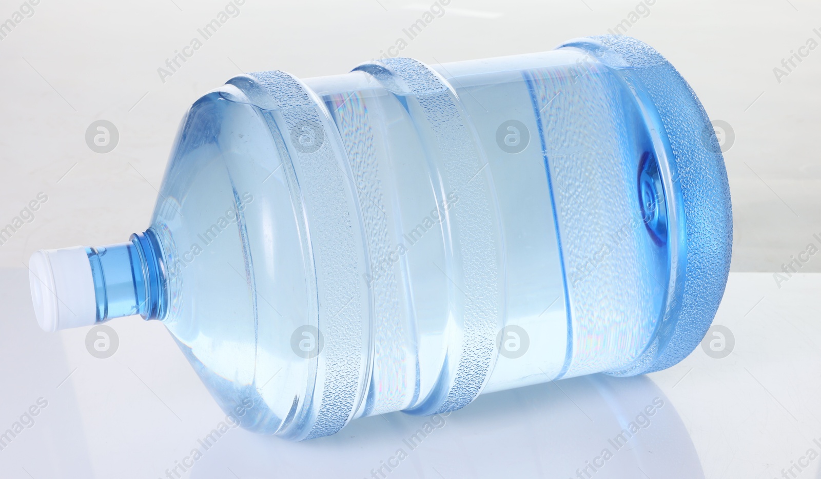 Photo of One cooler bottle with water on mirror table against white background, closeup