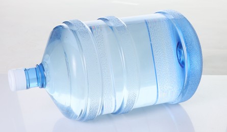Photo of One cooler bottle with water on mirror table against white background, closeup