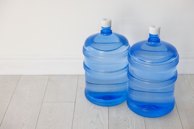 Photo of Cooler bottles with water on wooden floor near white wall. Space for text