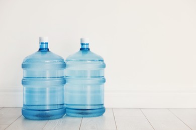 Photo of Cooler bottles with water on wooden floor near white wall. Space for text