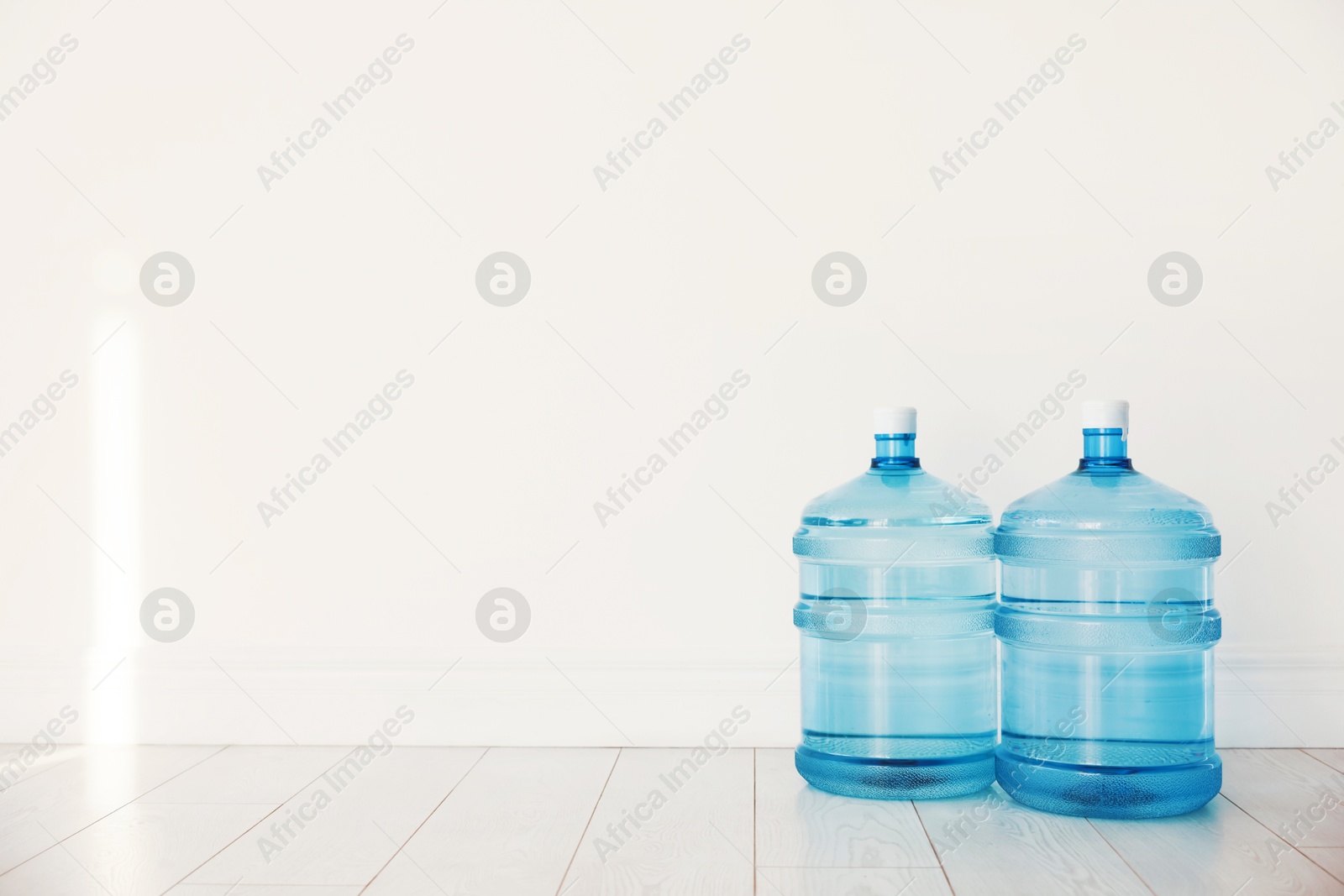 Photo of Cooler bottles with water on wooden floor near white wall. Space for text