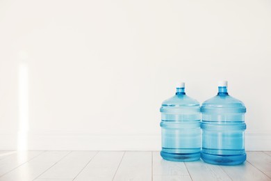 Photo of Cooler bottles with water on wooden floor near white wall. Space for text