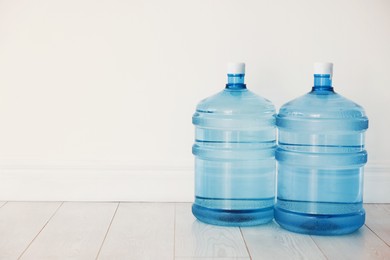Photo of Cooler bottles with water on wooden floor near white wall. Space for text