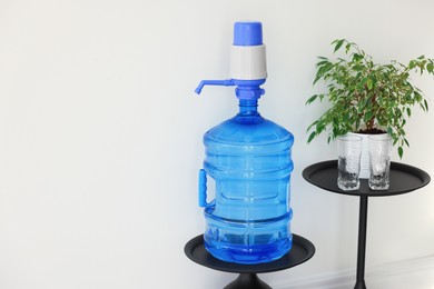 Photo of Cooler bottle with water, pump, glasses and houseplant near white wall. Space for text