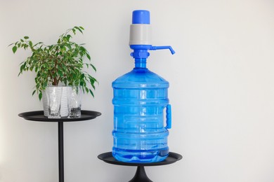 Photo of Cooler bottle with water, pump, glasses and houseplant near white wall. Space for text