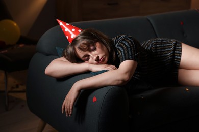Photo of Woman suffering from hangover on sofa in messy room after party