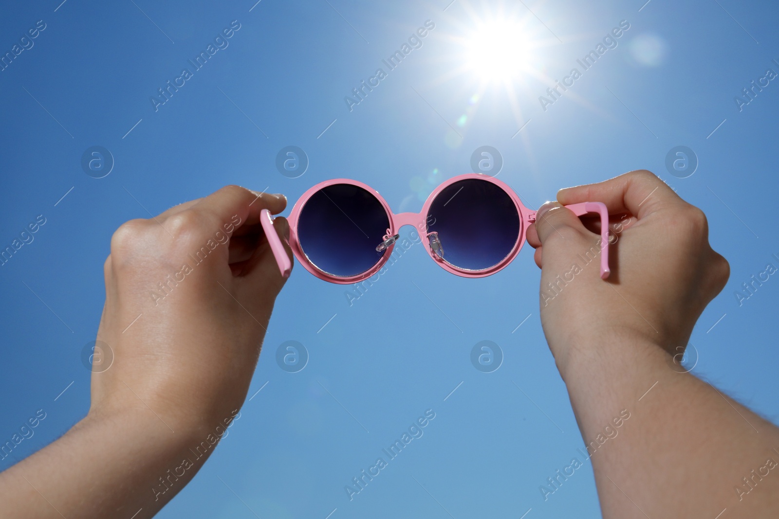 Woman holding stylish sunglasses against blue sky on sunny day, low angle view Photo of Woman holding stylish sunglasses against blue sky on sunny day, low angle view