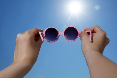 Photo of Woman holding stylish sunglasses against blue sky on sunny day, low angle view