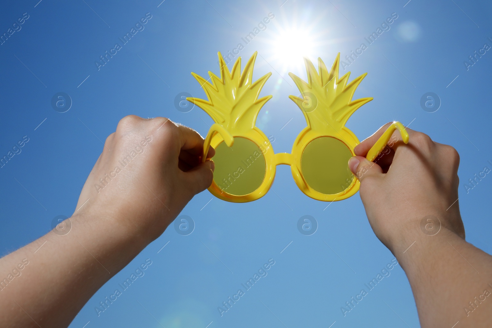 Woman holding funny sunglasses against blue sky on sunny day, low angle view Photo of Woman holding funny sunglasses against blue sky on sunny day, low angle view