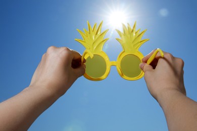 Photo of Woman holding funny sunglasses against blue sky on sunny day, low angle view