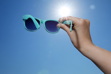 Photo of Woman holding stylish sunglasses against blue sky on sunny day, low angle view