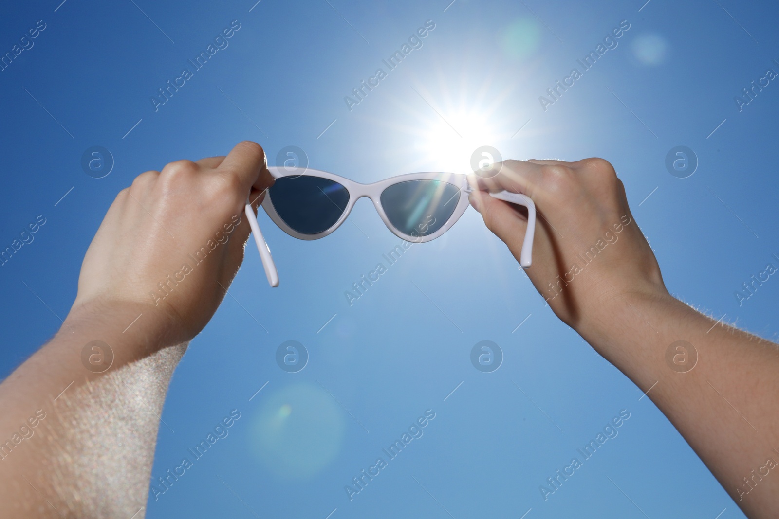 Woman holding stylish sunglasses against blue sky on sunny day, low angle view Photo of Woman holding stylish sunglasses against blue sky on sunny day, low angle view