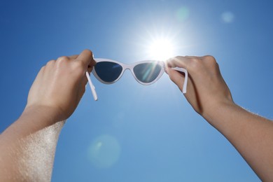 Photo of Woman holding stylish sunglasses against blue sky on sunny day, low angle view