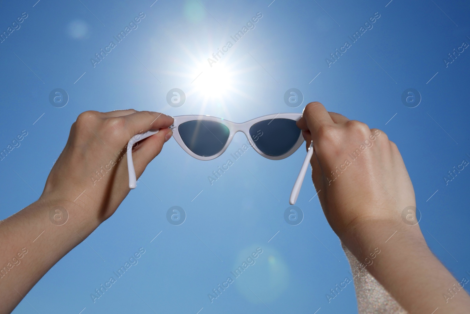 Woman holding stylish sunglasses against blue sky on sunny day, low angle view Photo of Woman holding stylish sunglasses against blue sky on sunny day, low angle view