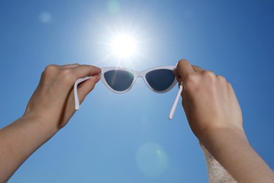 Photo of Woman holding stylish sunglasses against blue sky on sunny day, low angle view