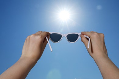 Photo of Woman holding stylish sunglasses against blue sky on sunny day, low angle view