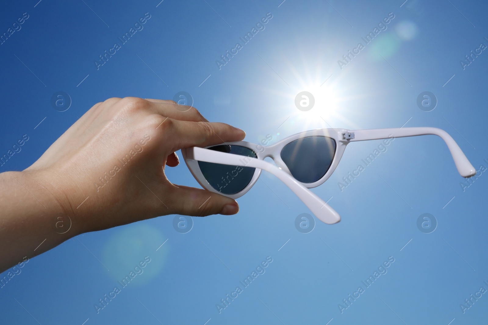 Woman holding stylish sunglasses against blue sky on sunny day, low angle view Photo of Woman holding stylish sunglasses against blue sky on sunny day, low angle view