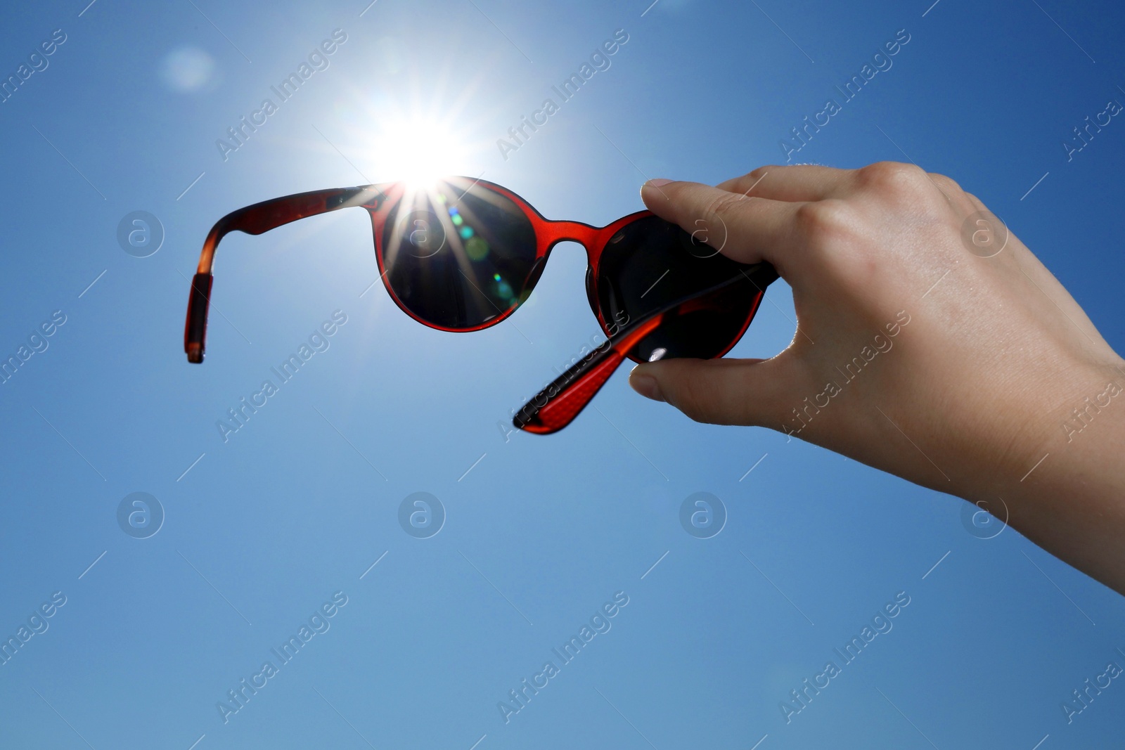 Woman holding stylish sunglasses against blue sky on sunny day, low angle view Photo of Woman holding stylish sunglasses against blue sky on sunny day, low angle view