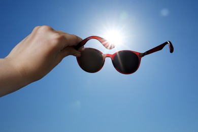 Photo of Woman holding stylish sunglasses against blue sky on sunny day, low angle view